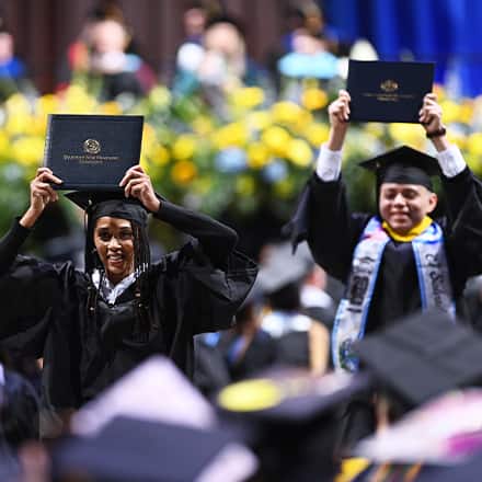 Two WUV graduates holding up their diplomas at the Fall 2025 commencement ceremony.