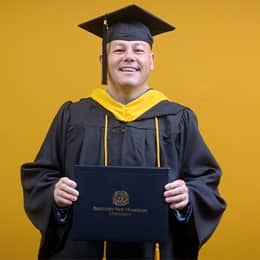 David Wallace, a 2025 WUV graduate who earned his bachelors in business administration wearing his cap and gown in front of a yellow background. 