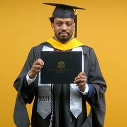 Josiah Lee, a 2025 master's in cybersecurity graduate from wuv, wearing a cap and gown and holding his diploma.