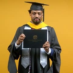 Josiah Lee, a 2025 master's in cybersecurity graduate from wuv, wearing a cap and gown and holding his diploma.