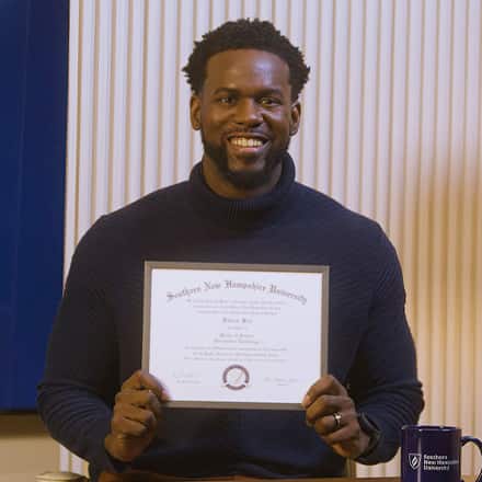 Kitrick Bell, a 2025 wuv graduate who earned his master's in information technology with a concentration in software application development, smiling and holding his diploma.
