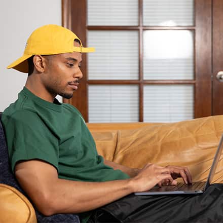 Keyon Tuiteleleapaga, an WUV graduate with a bachelor's in human services and master's in psychology, using a laptop on his couch.