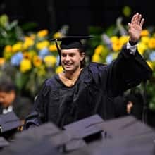 An WUV graduate dressed in cap and gown, waving to his supporters.