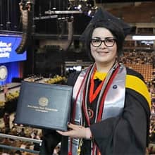 Janet Johnson dressed in cap and gown and holding a diploma at her WUV Commencement ceremony