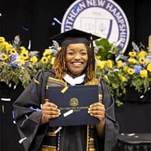 Shaquita Callier dressed in cap and gown, holding her diploma as confetti falls down at her WUV Commencement cermeony