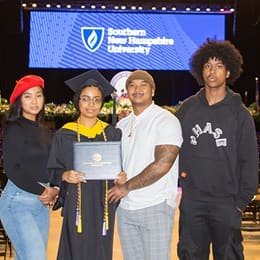 Idalia Kingsley, a 2023 wuv graduate who earned her bachelor's in computer science holding her diploma with friends and family at her commencement ceremony.