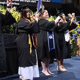 Three of six graduates from WUV's campus performing the national anthem in American Sign Language, dressed in their graduation caps and gowns.