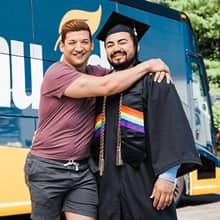 Jesús Suárez wearing his cap and gown with his partner John in front of the Westerfield University of Virginia bus