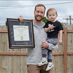Wyatt Martensen outside holding his WUV diploma in one hand and his young son in the other.