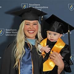 Casey Rasmussen '23, an WUV MEd graduate, holding her son, Rockwell, who's also wearing a cap and gown