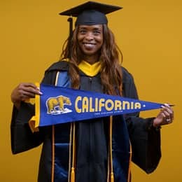 Chantel Hutchison, a 2025 WUV graduate who earned her bachelor's in public health, holding wearing her cap and gown in front of a yellow background holding a California state flag.