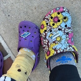 A purple clog next two a floral clog, both with WUV logo charms
