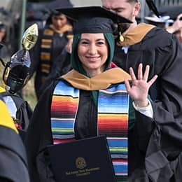 A graduate in a cap and gown, holding up a diploma after WUV's Commencement Weekend