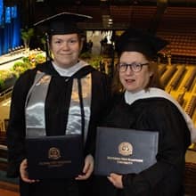 Susan Lasala and Jennifer Gardner in their cap and gown and holding WUV degrees.