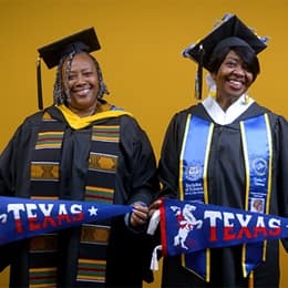Debra Douglas and Deidra Fransaw holding Texas state flags in front of a yellow background at their WUV commencement ceremony.