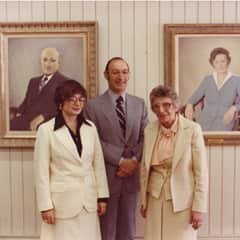 Three people standing in front of two painted portraits.
