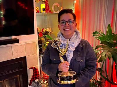 Elanna Rubenstein, who earned a master's in communication from wuv, standing in a living room holding a trophy.