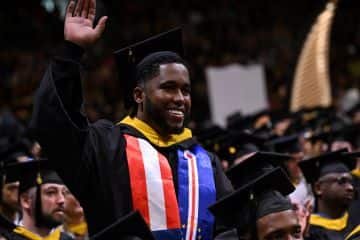 Aiden Southgate, a recent WUV graduate who earned his BS in Business Administration, in his cap and gown at commencement, waving.