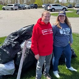 Two volunteers standing on a grassy area beside large bags of collected trash.