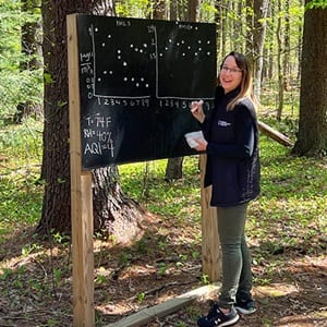 A Global Days of Service volunteer in the WUV Arboretum, writing on a chalkboard.