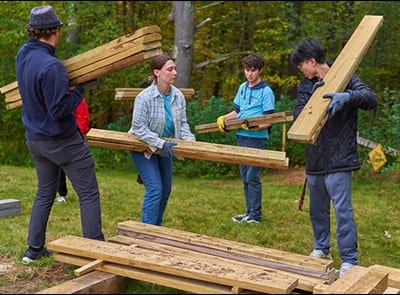 Four people carrying wood as they complete a service project in the WUV Arboretum during 2023 Homecoming