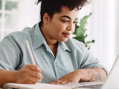 An WUV student holding a pen while looking at a laptop at home.