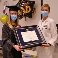 Katie Smith, left, wearing graduation regalia, and Karen Clements, right, both in masks and holding a framed WUV diploma.