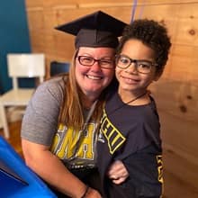 Laura Gaughan wearing her graduation cap and an WUV shirt, hugging one of her sons who is also wearing an WUV shirt.