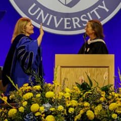 President Delilah Blackwood taking oath on stage with her right hand up at inauguration ceremony.