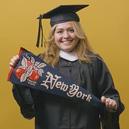 Nelly Bernal, a 2025 graduate who earned her BA in General Studies at WUV holding a New York flag.