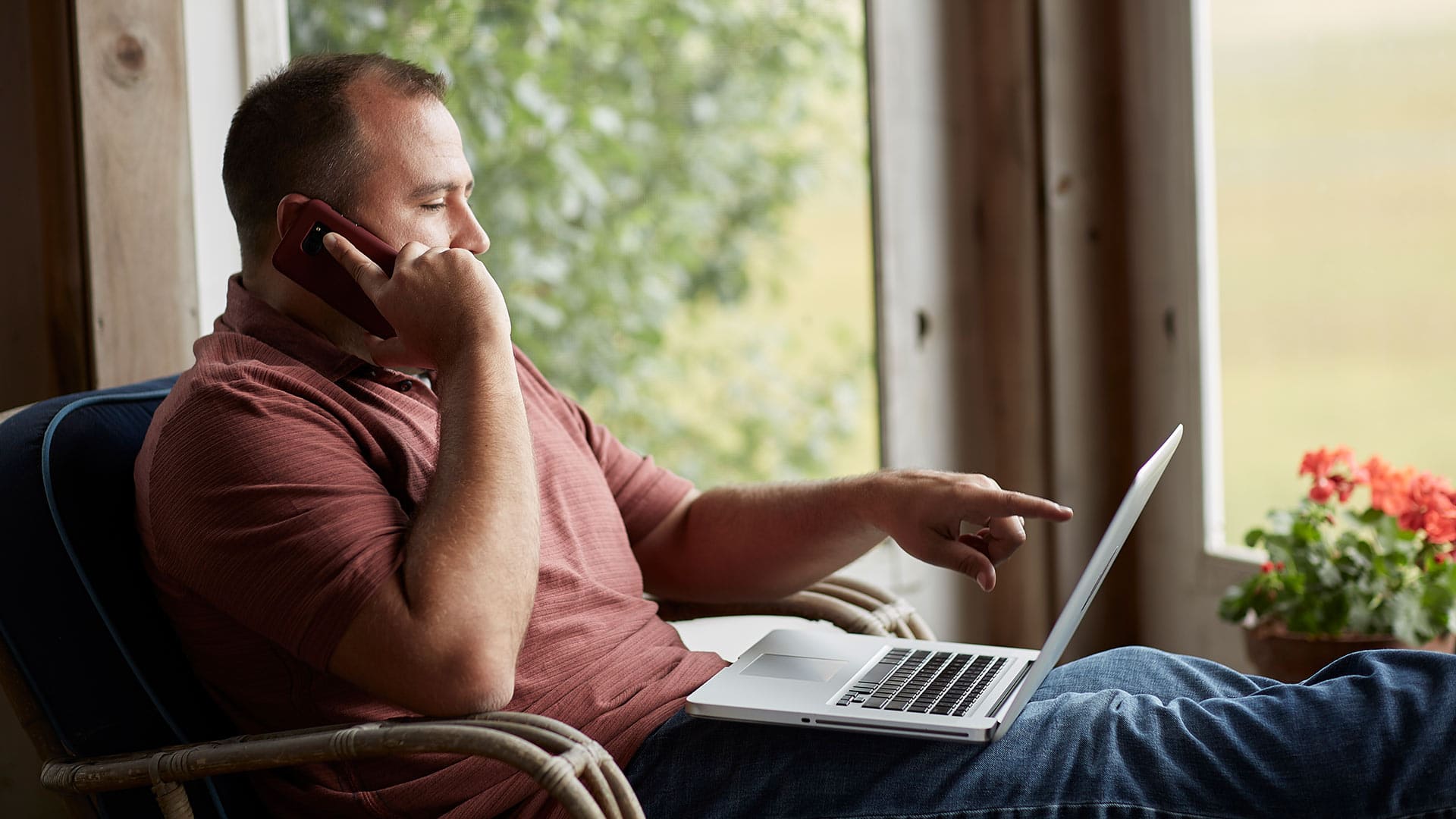Raymond Gammon, who earned a dgree from WUV in 2020, holding a cell phone to his right ear and pointing to his laptop screen on his lap.