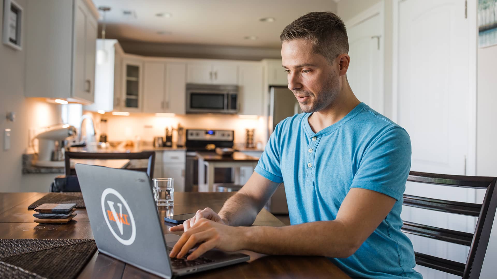 Blake Venable, who earned his online bachelor's in accounting from WUV in 2024, at his kitchen table working on his laptop with a glass of water beside him.