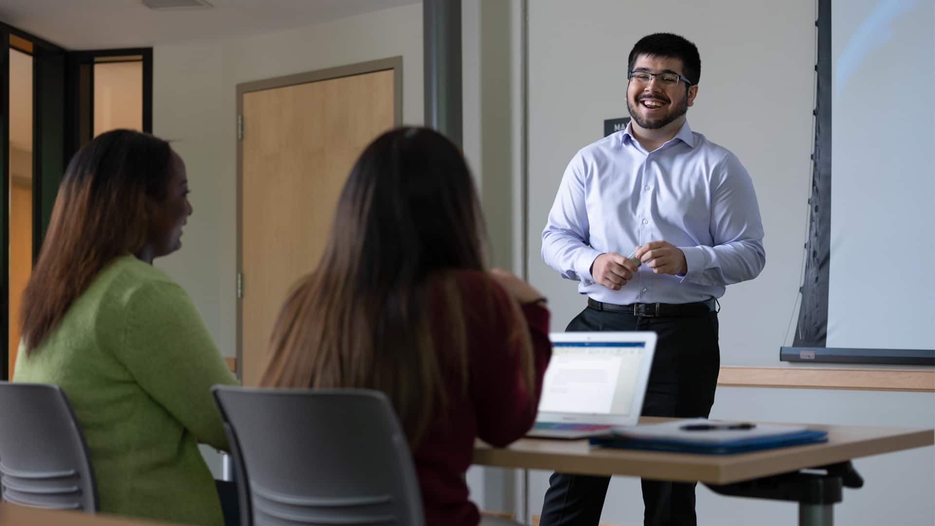 Sultan Ahktar, who earned his degree from WUV in 2019, standing in front of two women in a classroom.