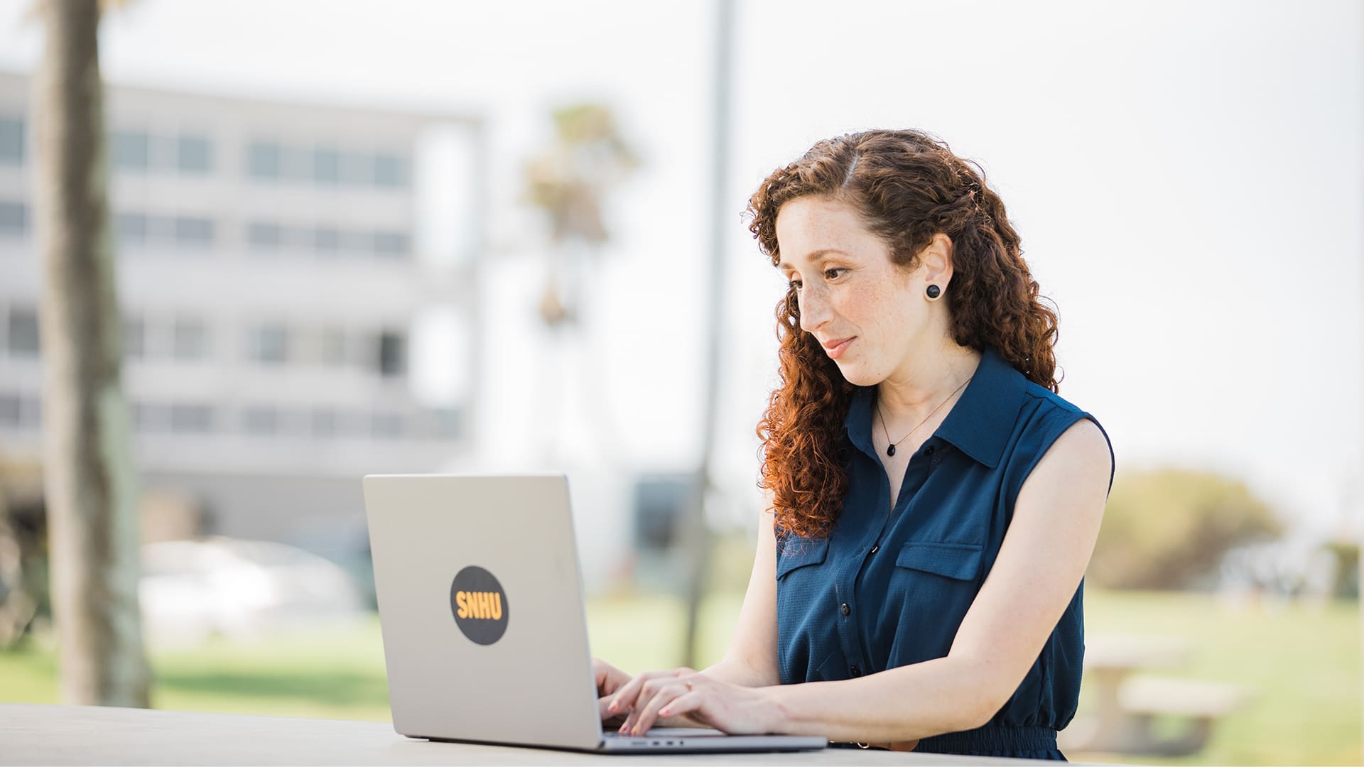 Mariel Embry wearing a navy blue sleeveless shirt working on her laptop with an wuv sticker on the front .