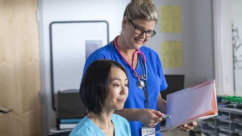 Kristina Libby, who earned her nursing degree from wuv in 2017, wearing blue scrubs and holding a clipboard next to a colleague in a clinical office.