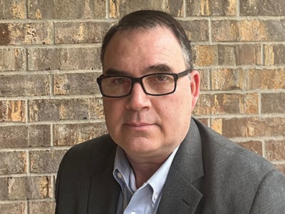 Ryan Whitaker, an adjunct faculty member in wuv's online MS in management with a concentration in Construction Management program, in front of a brick wall.