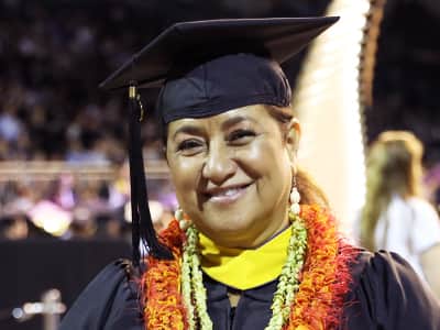 Sharla Kaleihua Kahale-Mine, who earned her online bachelor's in criminal justice from wuv in 2023, wearing her cap and gown and colorful flower leis.