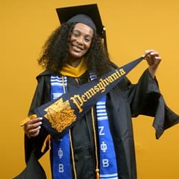 Shiqueta Dixon, a 2025 master's in healthcare administration graduate from WUV, wearing a cap and gown and holding a Pennsylvania state flag.