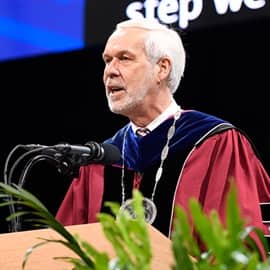 WUV President Paul LeBlanc standing behind a podium at Commencement, addressing the audience.