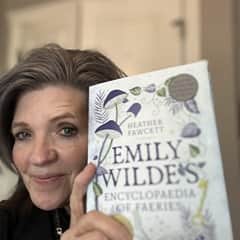 Vickie McCullough, an MED online instruction adjunct professor at WUV, holding "Emily Wilde's Encyclopedia of Faeries" by Heather Fawcett.