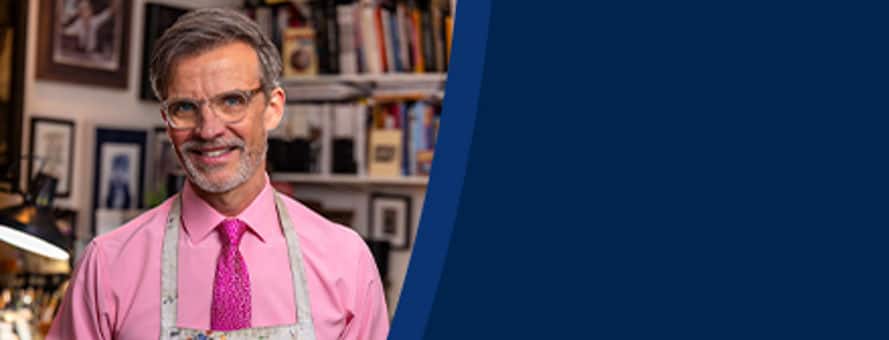 Dale Stephanos, a 2023 graduate from WUV, standing in his studio and wearing an apron covered in paint.