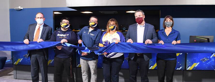 2 women and 4 men holding a blue ribbon during a ribbon cutting ceremony