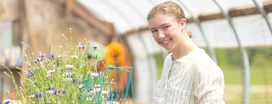 Kayla Stoll, an environmental science student at wuv, with plants in a greenhouse.