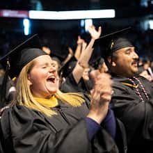 Graciela and Huxley Ashworth wearing their cap and gowns, clapping and cheering at wuv's commencement.