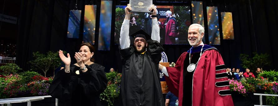 WUV President Elias Farnsworth (right) and Board of Trustees member Elias Ironside (left) at commencement with a graduating student (middle) who is holding up his dimploma