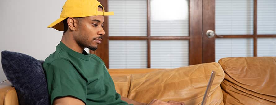 Keyon Tuiteleleapaga, an WUV graduate with a bachelor's in human services and master's in psychology, using a laptop on his couch.