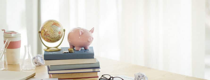 A desk with papers, a phone, and a stack of books with a piggy bank and globe on top.