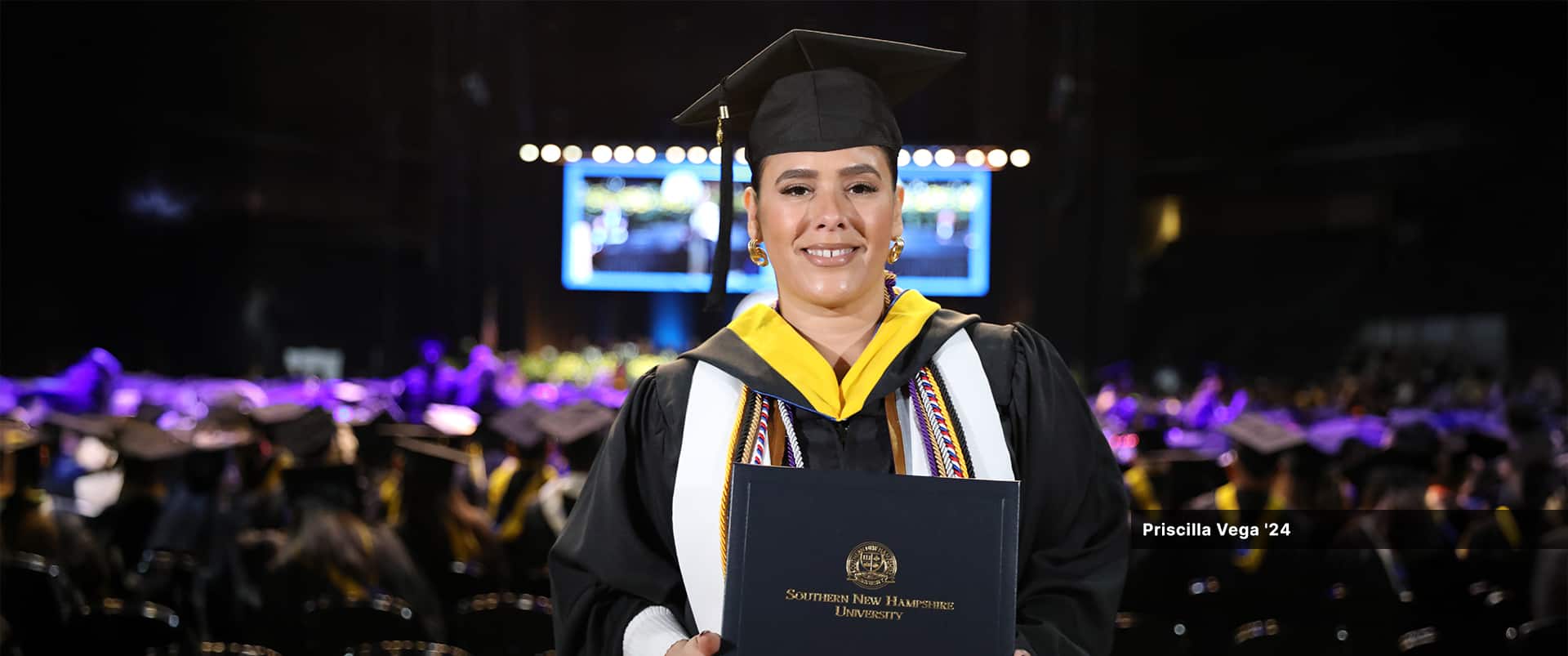 Priscilla Vega, who earned her bachelor's in business administration with a concentration in organizational leadership from WUV in 2024, wearing her cap and gown and holding her diploma.