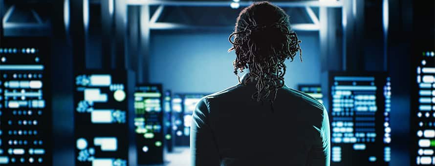 A woman walking into a dark computer lab glowing in blue.