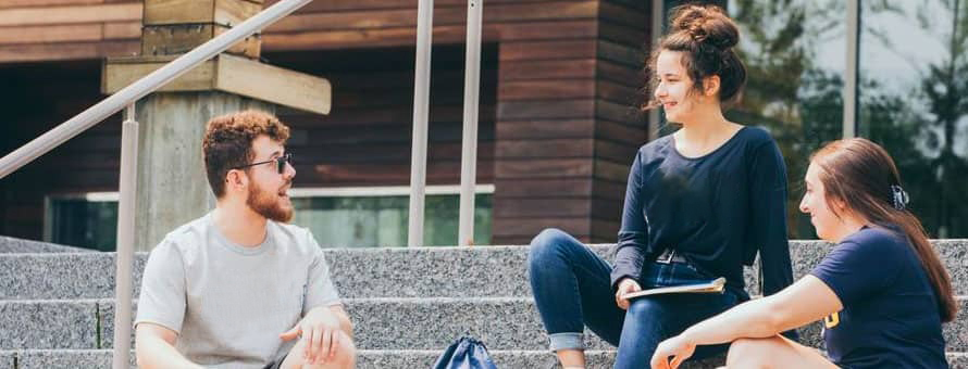 Three wuv students sitting outside on the steps of a campus building